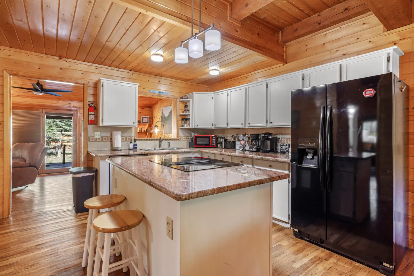 Kitchen with wood-paneled walls and ceiling, white cabinetry, a center island with barstools and cooktop, and a black refrigerator.