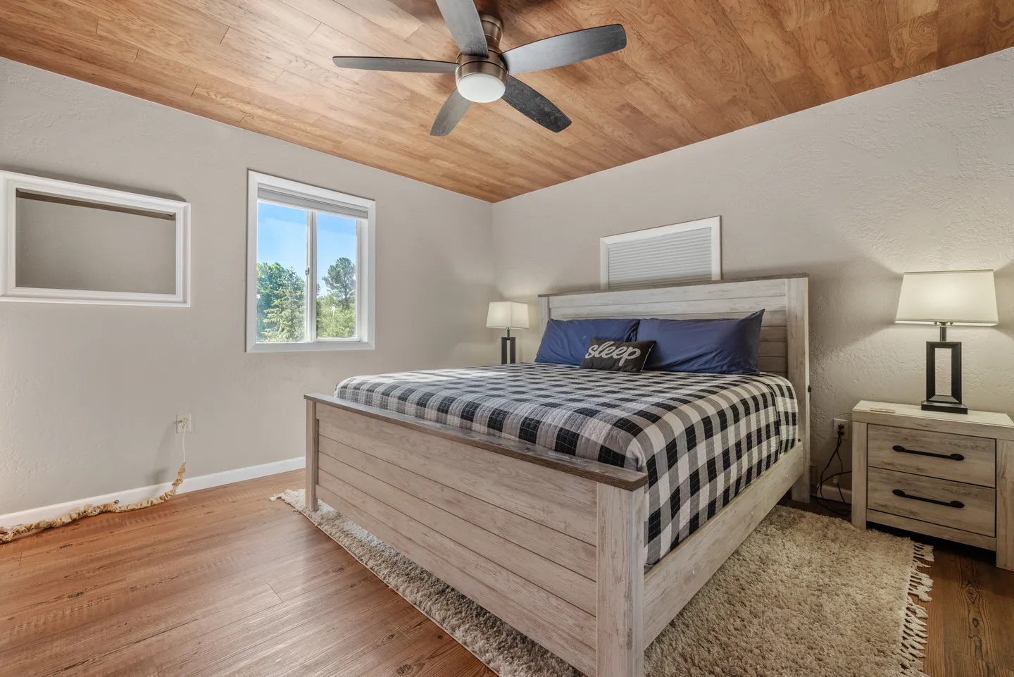 Bedroom featuring a wooden plank ceiling, ceiling fan, wood-style flooring, and a wooden bed frame dressed in buffalo check bedding.