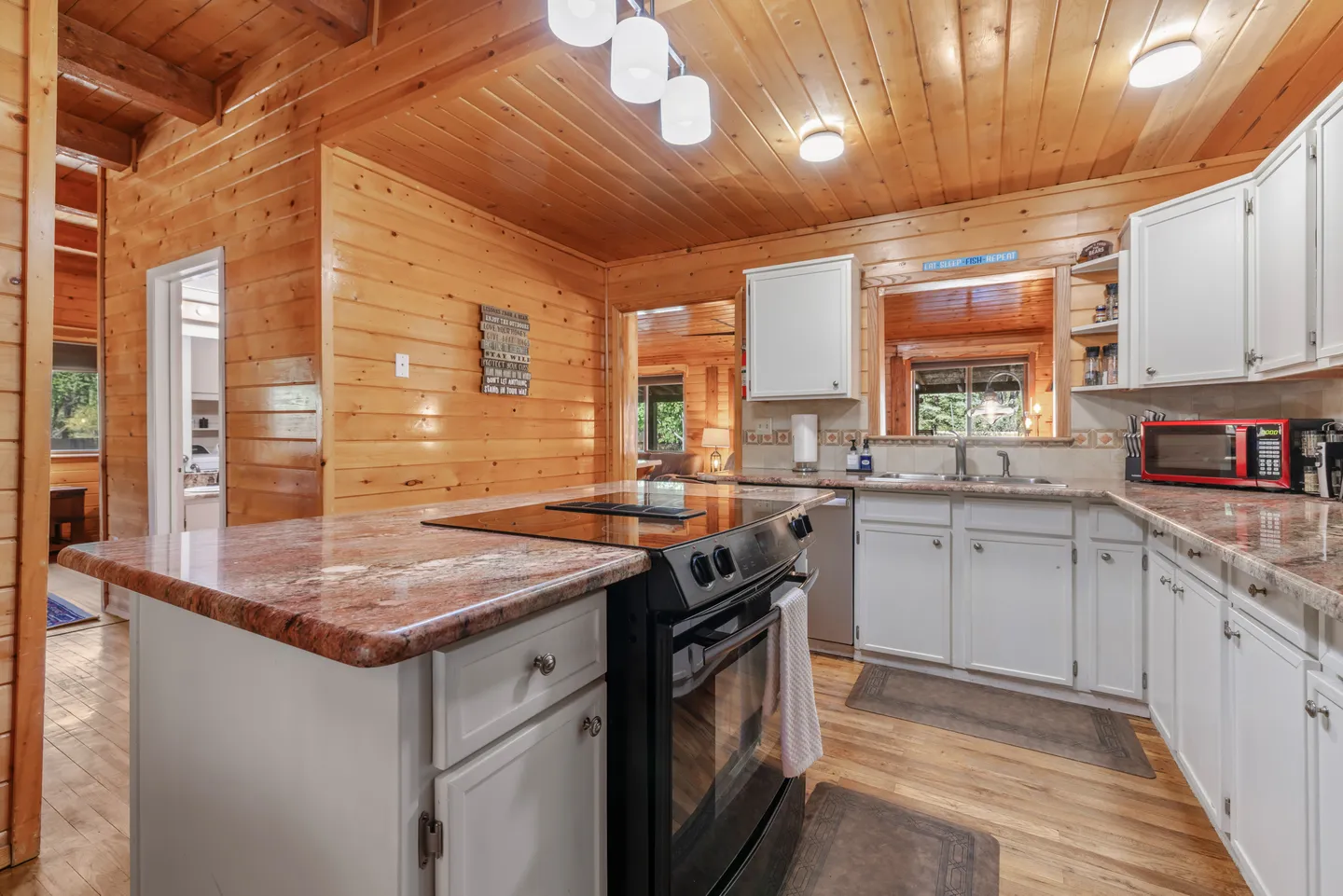 Kitchen with wood-paneled walls and ceiling, white cabinetry, dark cooktop island, and speckled countertops.