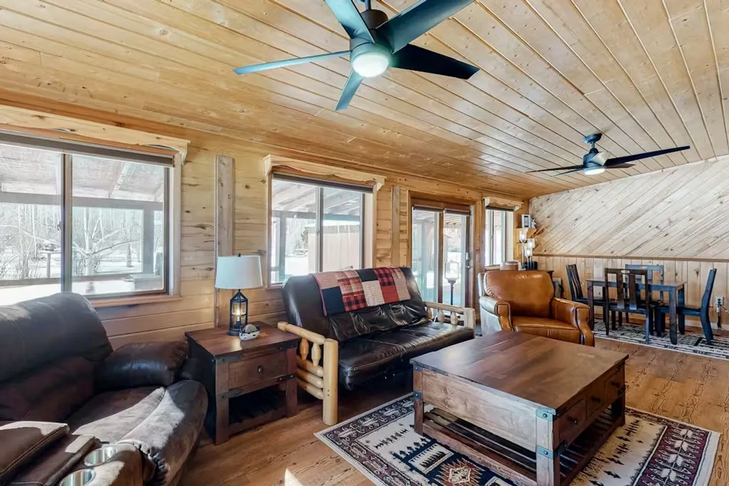 Living room with wood-paneled walls and ceiling, leather seating, a coffee table, and a dining table in the background.