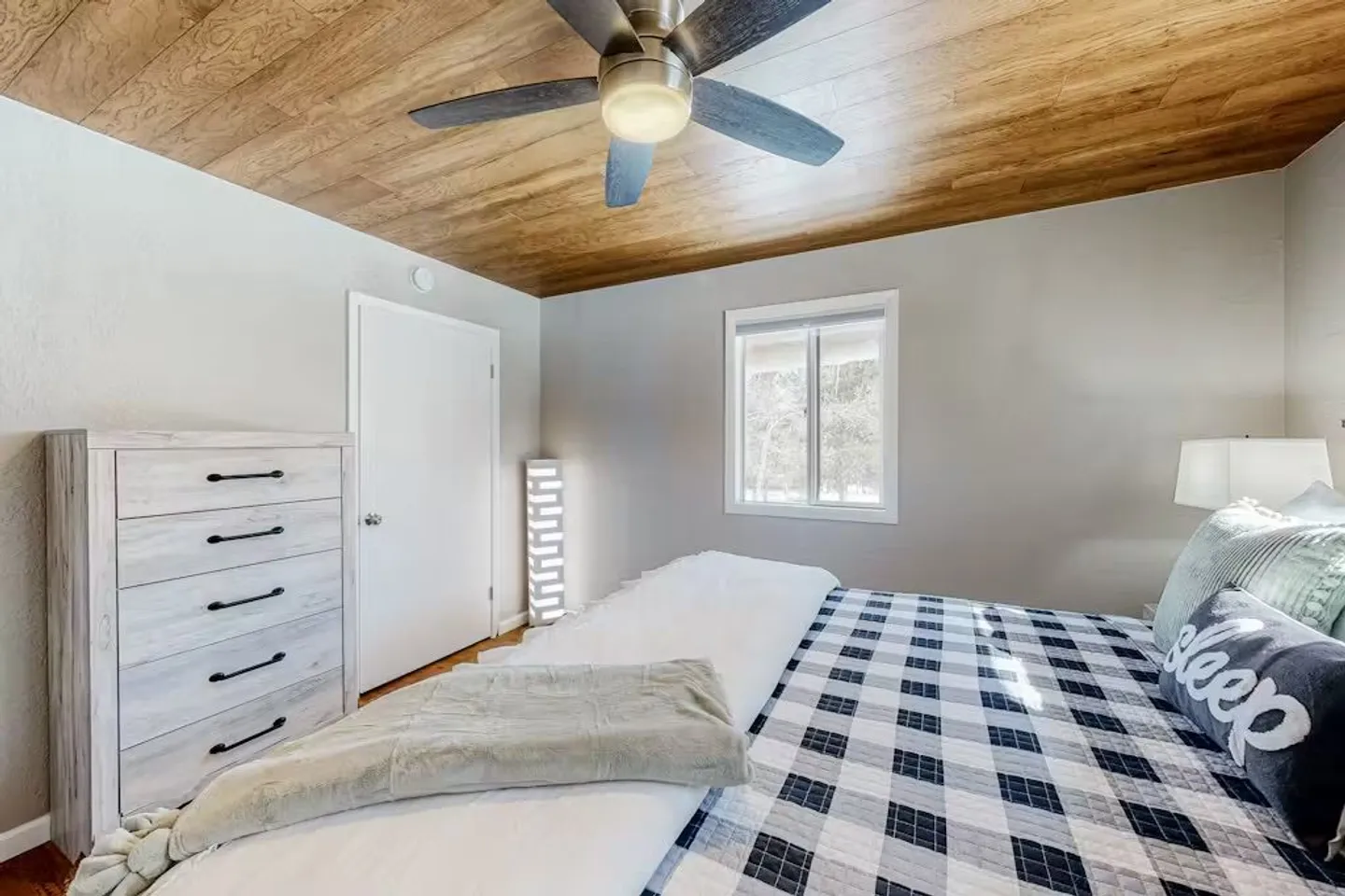 Bedroom with a wood-paneled ceiling, a ceiling fan, a bed with plaid bedding, and a light-colored dresser.