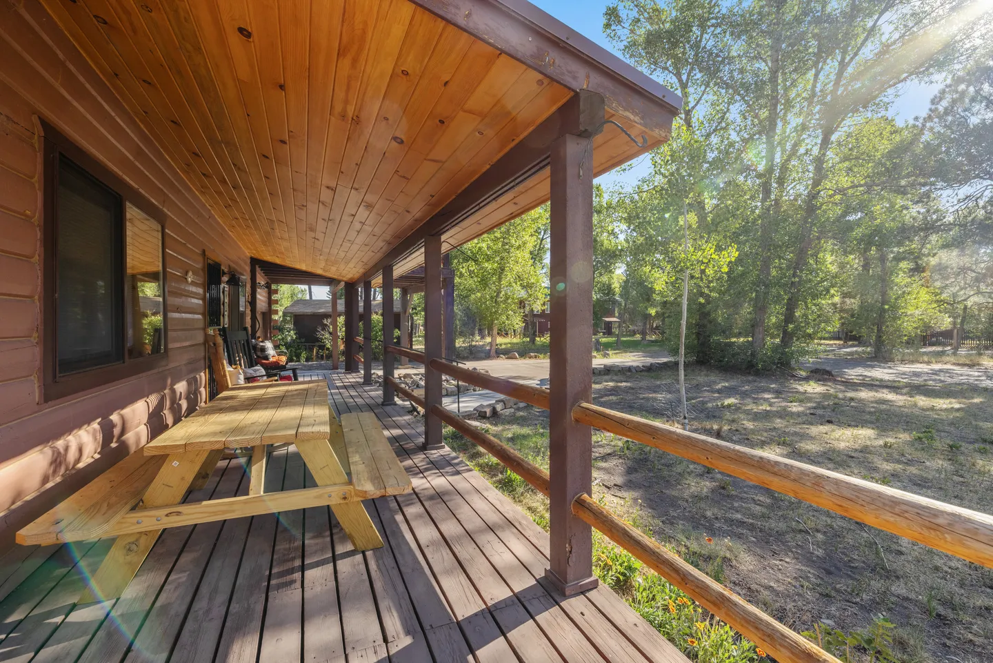 A covered wooden porch with a picnic table looking out toward tall trees and a yard.