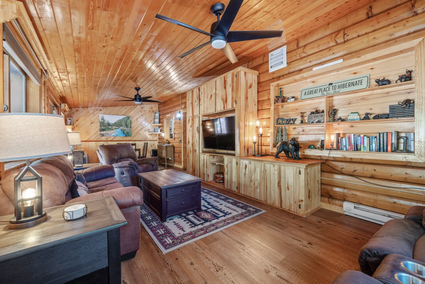 Living room with wood-paneled walls and ceiling, a ceiling fan, a brown sofa, a television cabinet, and built-in shelving.