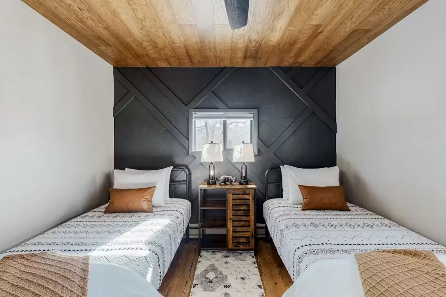 Bedroom with two twin beds, a wood-plank ceiling, and a dark geometric accent wall behind a small nightstand.