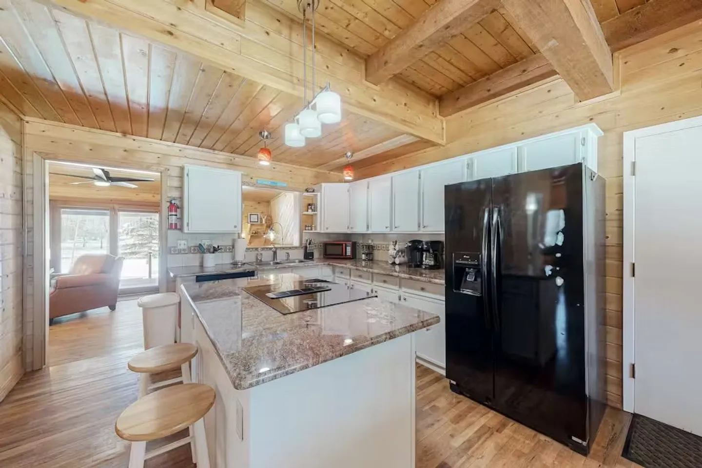 Kitchen with white cabinetry, granite countertops, an island with a built-in cooktop and barstools, black refrigerator, and wood-paneled ceiling.