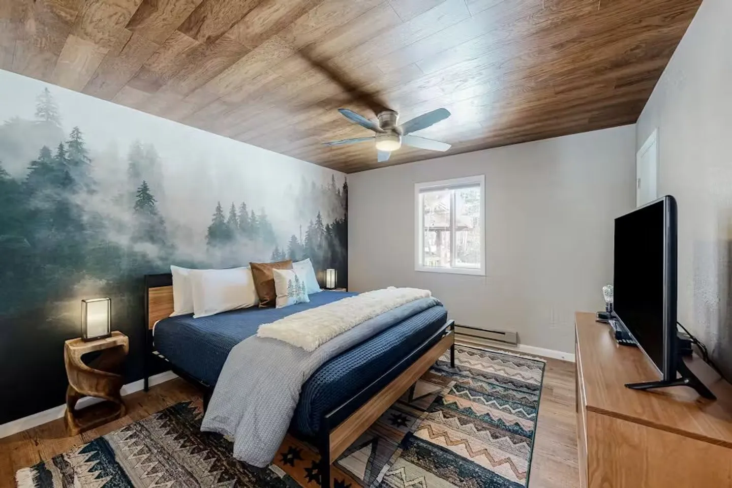 Bedroom featuring a forest wall mural behind the bed, wood-paneled ceiling with a ceiling fan, and a flat-screen TV.