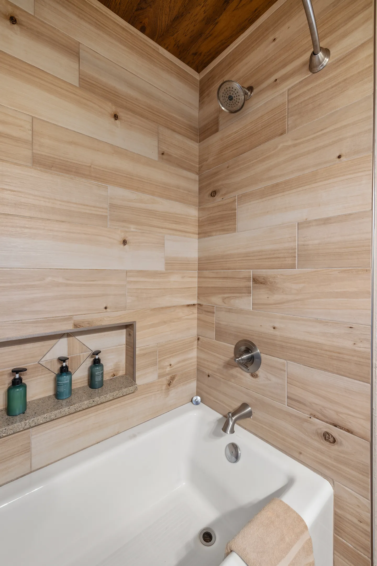Bathtub and shower combo featuring light wood-look wall tiles, brushed nickel fixtures, and a recessed toiletry niche.