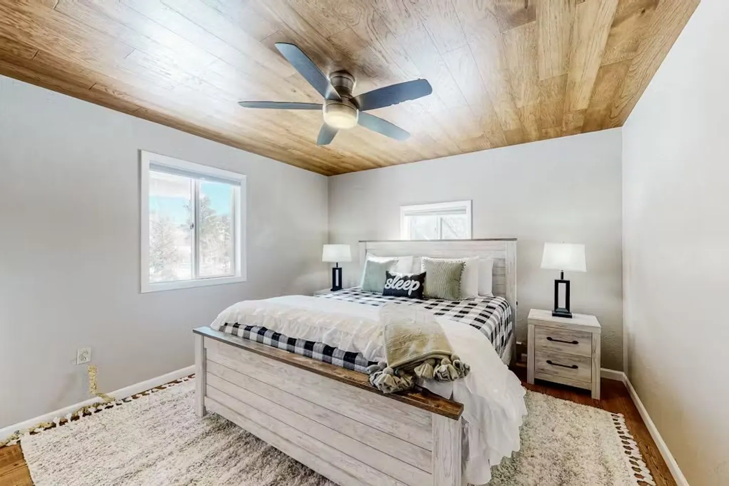 Bedroom featuring a wood-plank ceiling with a ceiling fan, a rustic wood bed frame, nightstands with lamps, and an area rug.