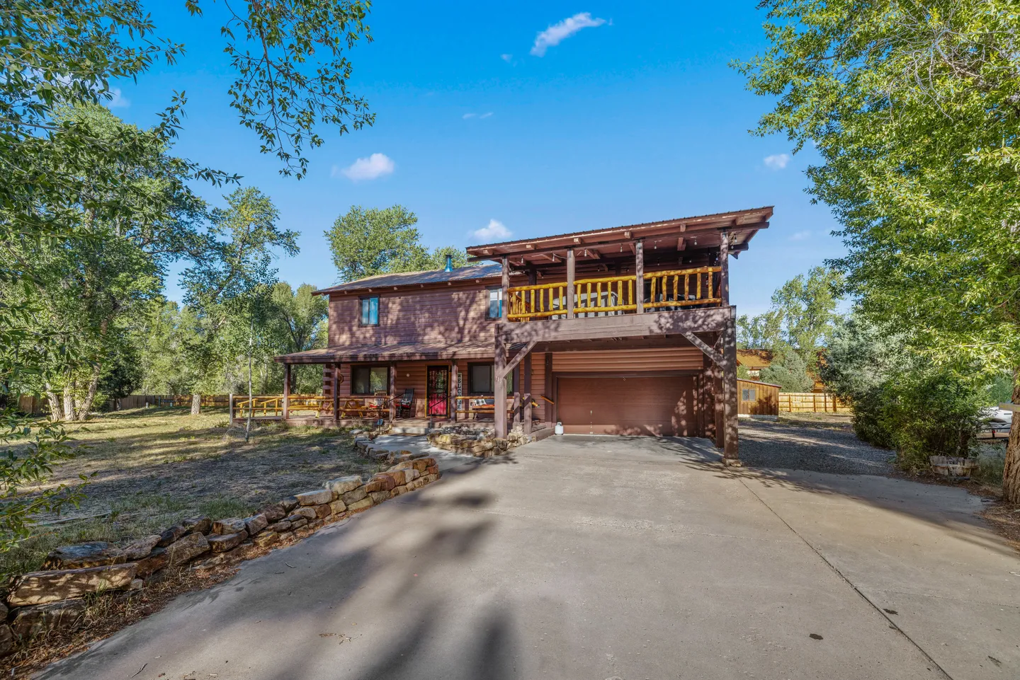 Exterior front view of a two-story log-style home with an attached garage, upper balcony, and concrete driveway.