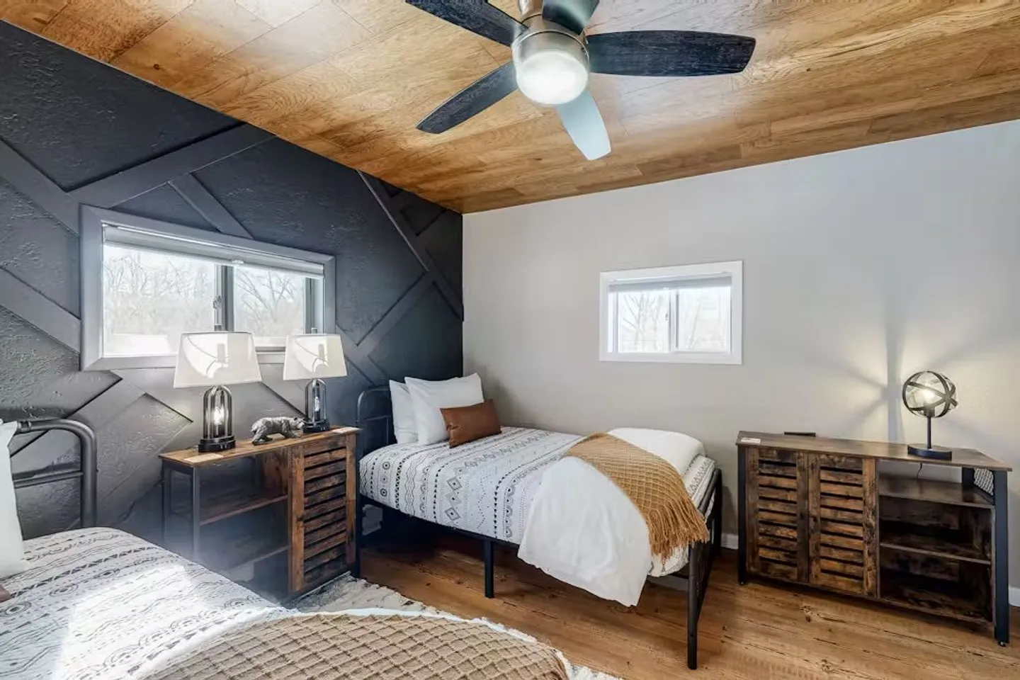 Bedroom featuring twin beds with metal frames, rustic wooden nightstands, a wood-paneled ceiling, and a dark accent wall with geometric molding.