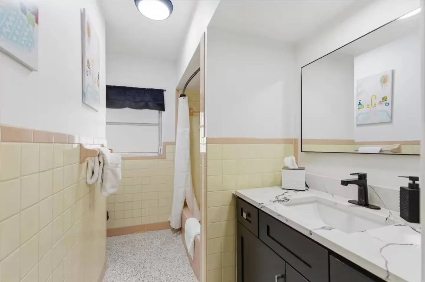 Bathroom featuring a dark vanity with a white marbled countertop, mirror, light yellow wall tiles, and a shower-tub combo.