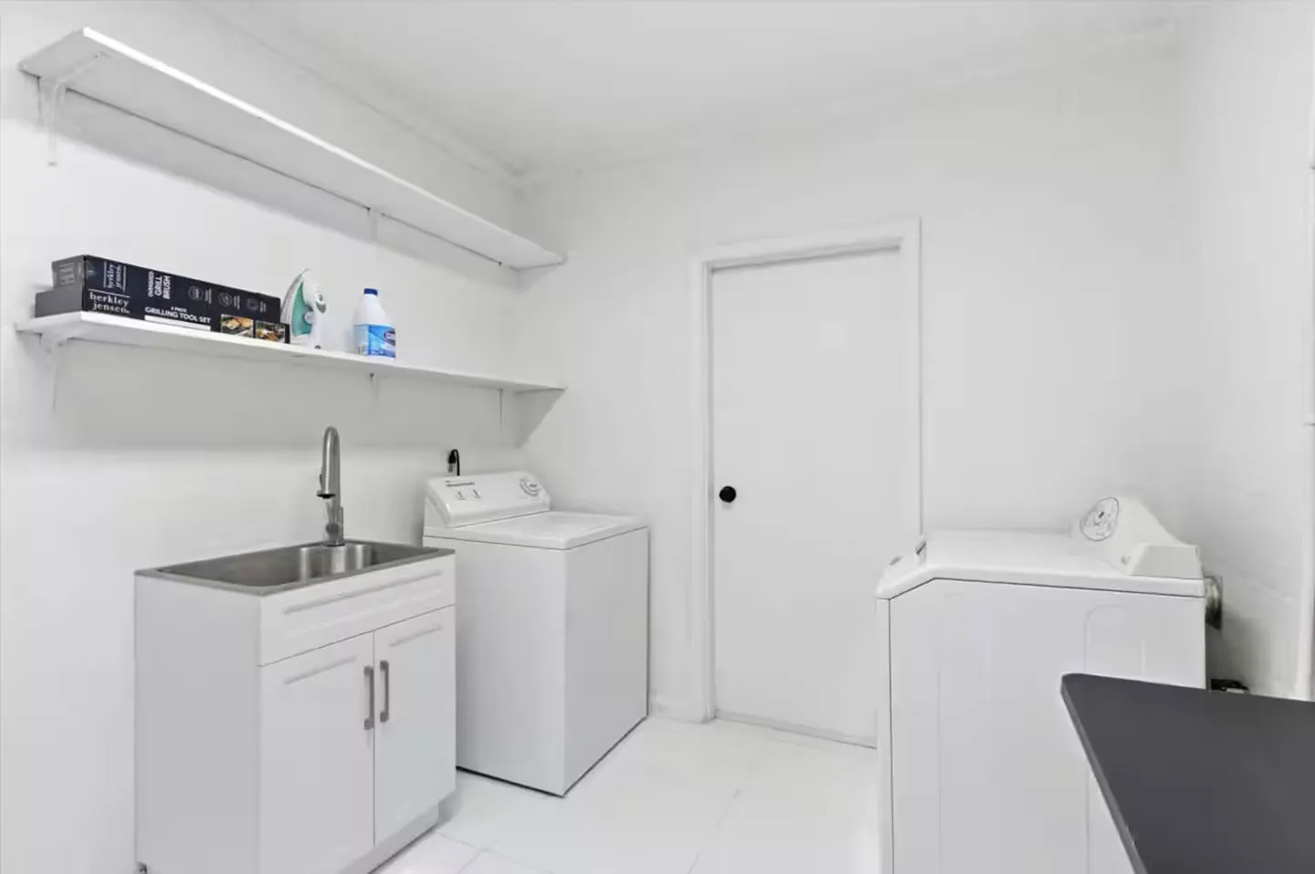 White laundry room with a utility sink cabinet, washer, dryer, and wall-mounted shelves.