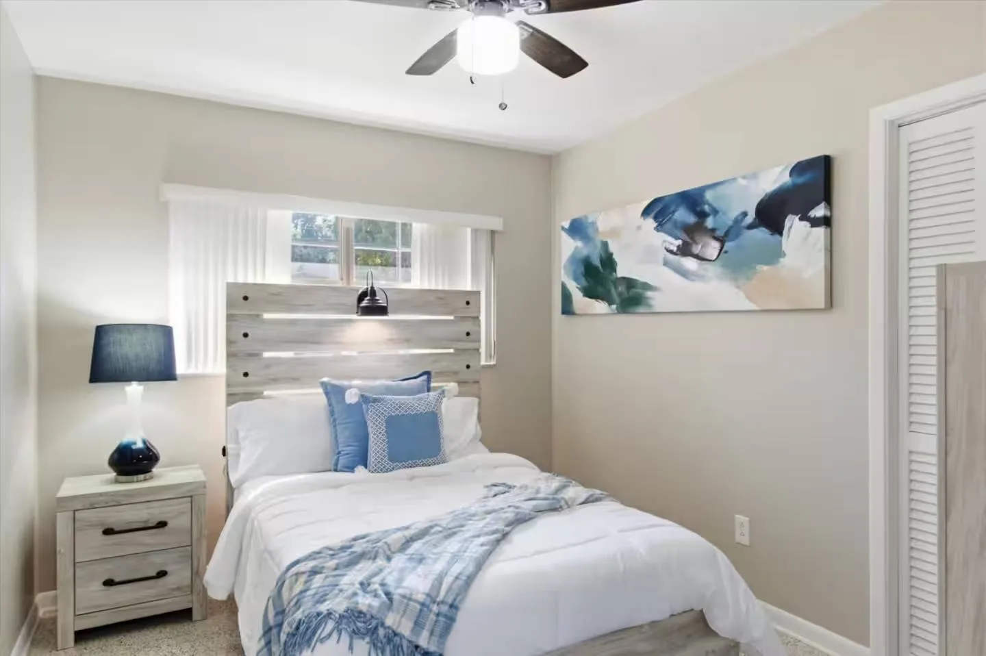 Bedroom with a single bed featuring a wooden slat headboard, a bedside nightstand with a lamp, abstract wall art, and a ceiling fan.