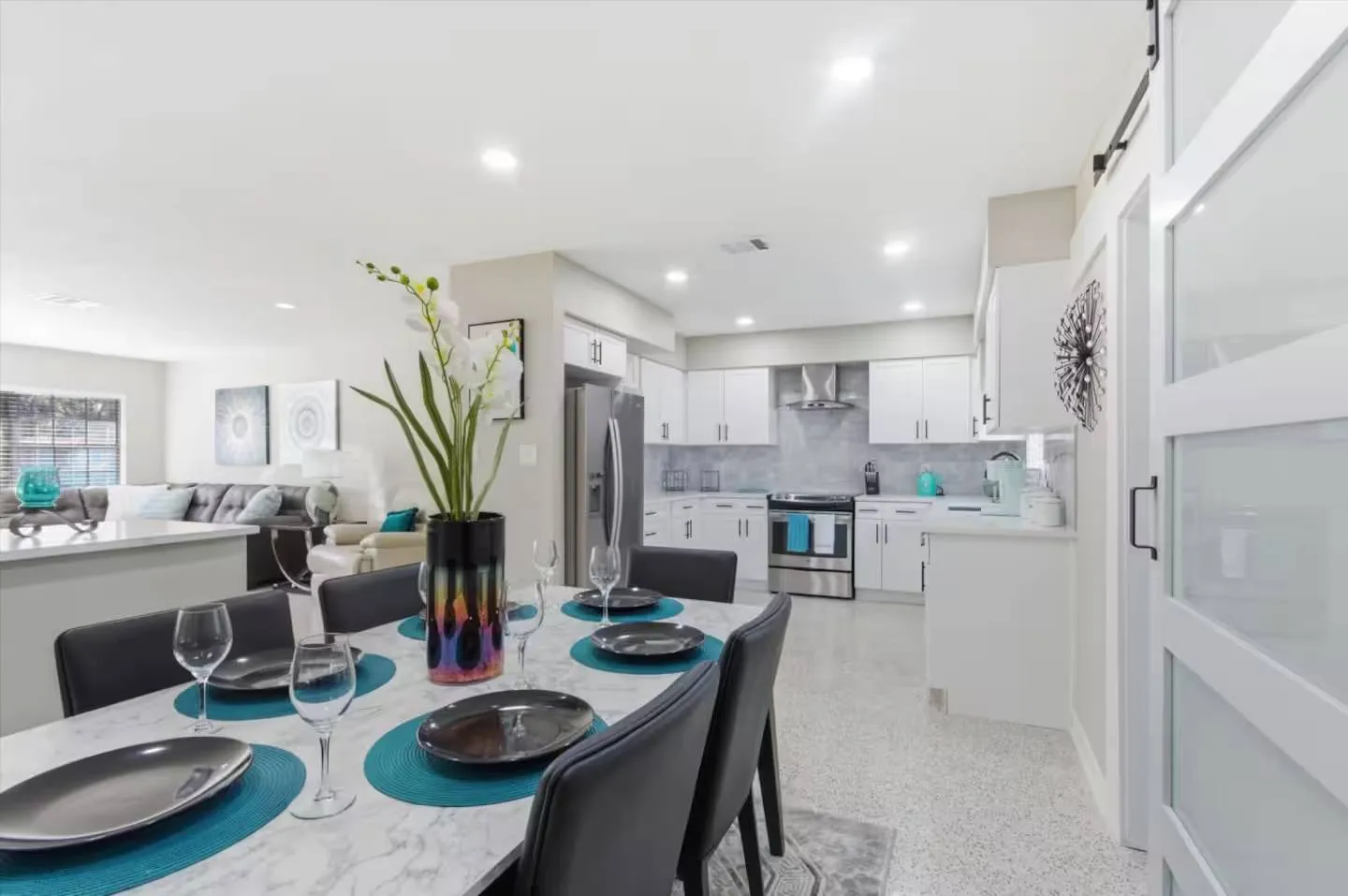Dining table set for a meal leading into an open-concept kitchen with white cabinets and stainless steel appliances.