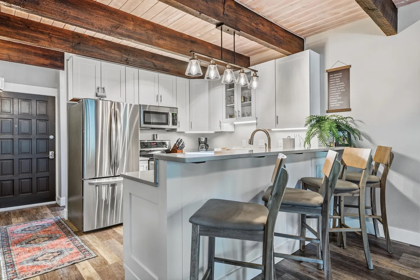 Kitchen with white cabinetry, stainless steel appliances, a breakfast bar with high-top barstools, and exposed dark wood ceiling beams.