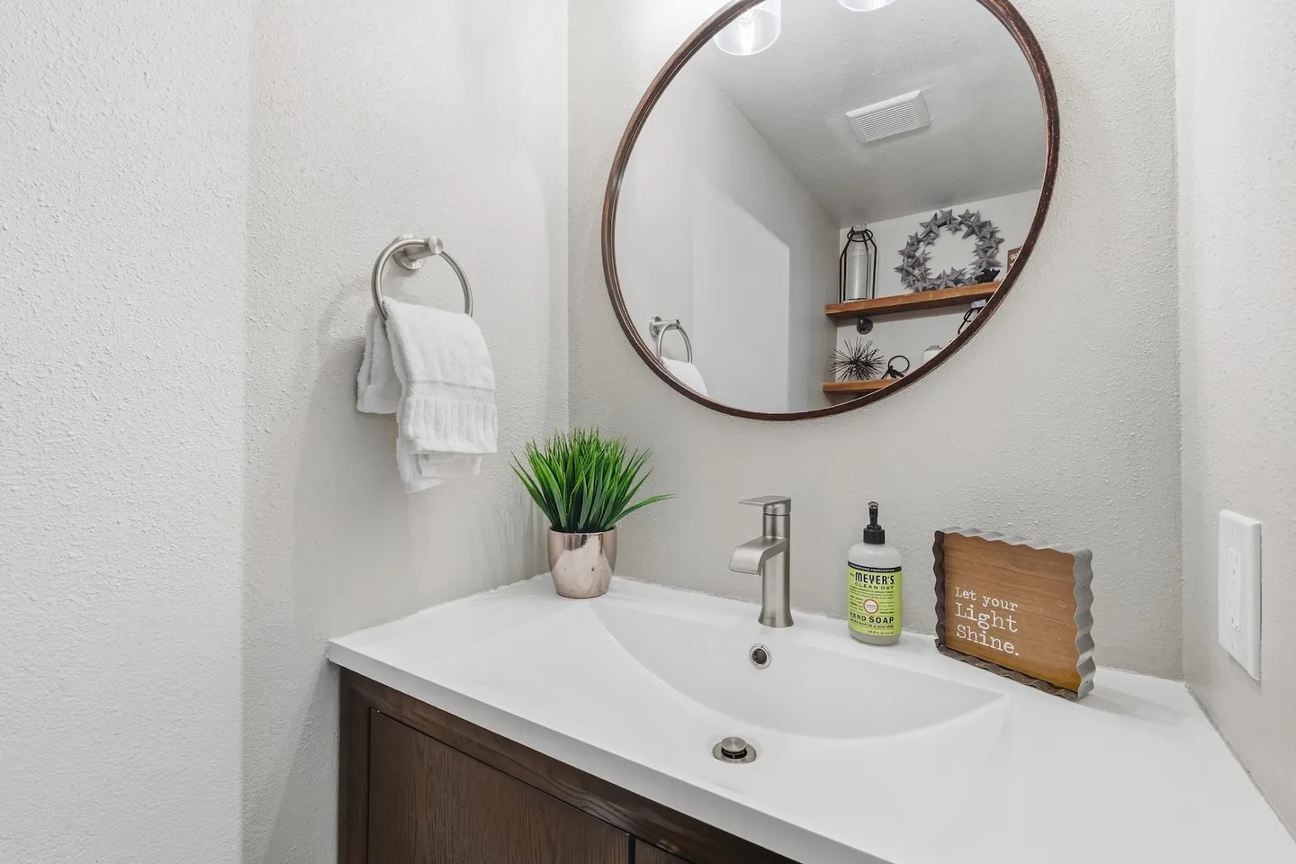 Bathroom vanity with a white molded countertop sink, modern faucet, round wall mirror, and decorative accents.