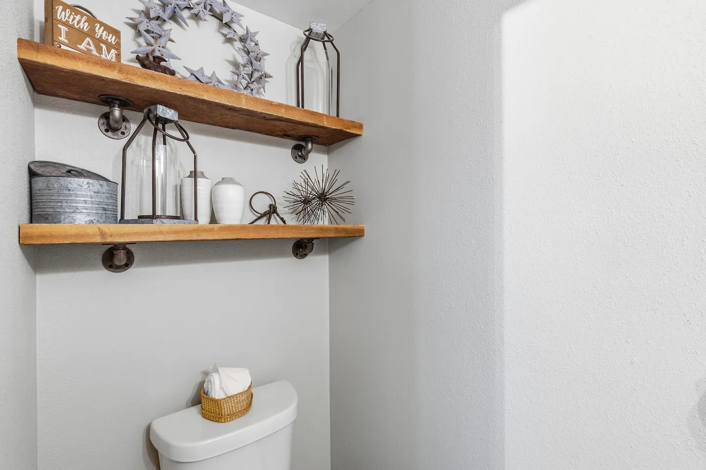 Floating wooden shelves with industrial pipe brackets mounted over a toilet tank in a bathroom nook.