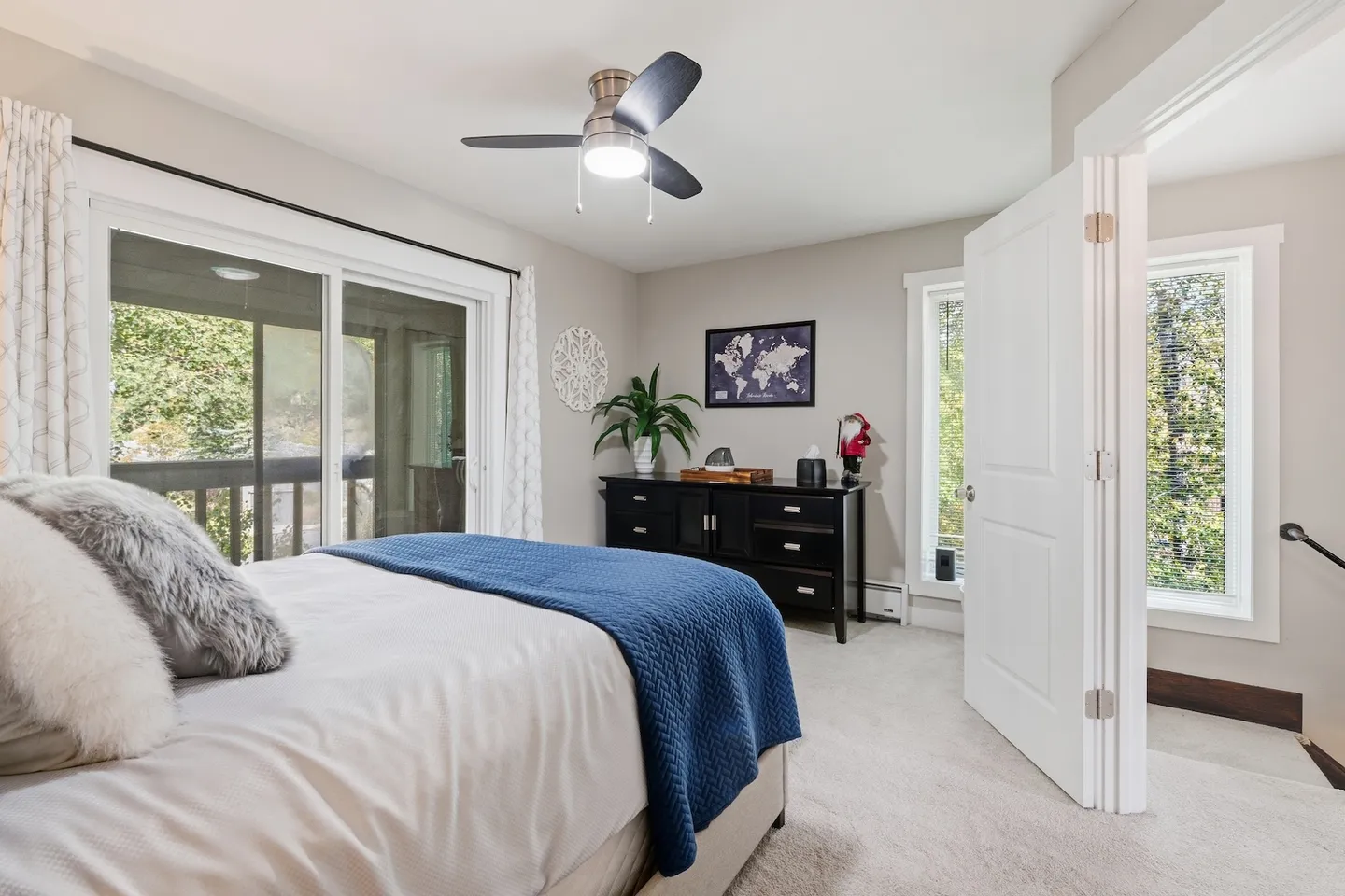 Bedroom with a bed dressed in white and blue, sliding glass doors leading to a balcony, a ceiling fan, and a black dresser.