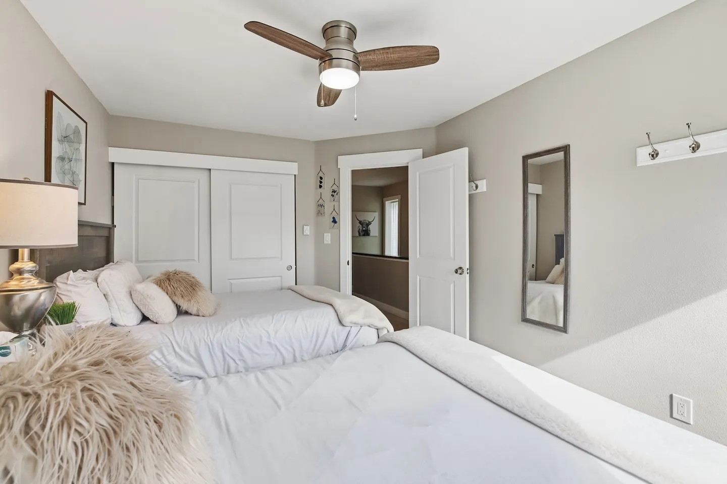 Bedroom with two beds made up in white linens and furry pillows, a ceiling fan, closet sliding doors, and an open doorway.