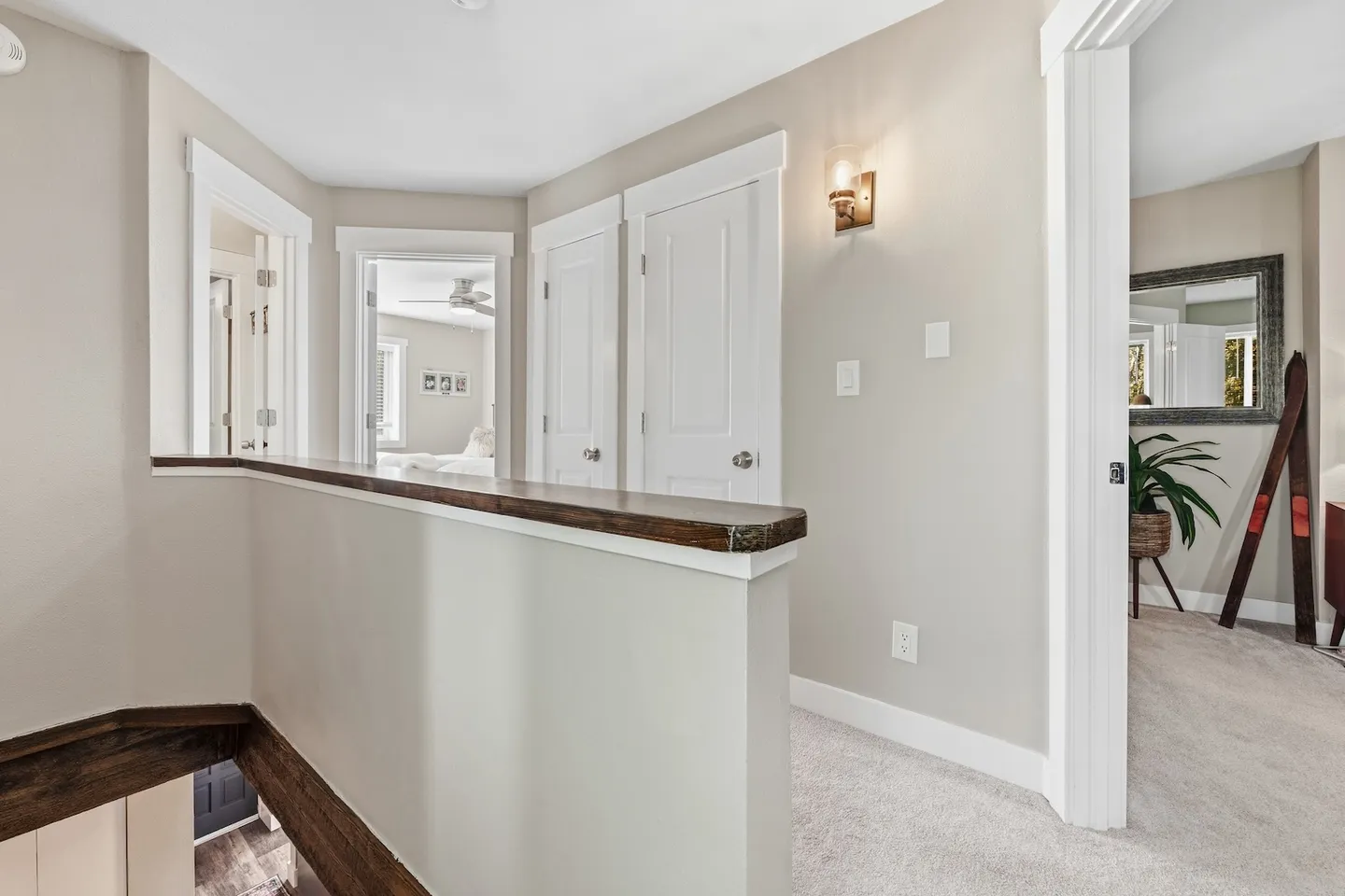 Upstairs hallway with carpeted flooring, a half-wall railing with dark wood trim, and doors leading to bedrooms.