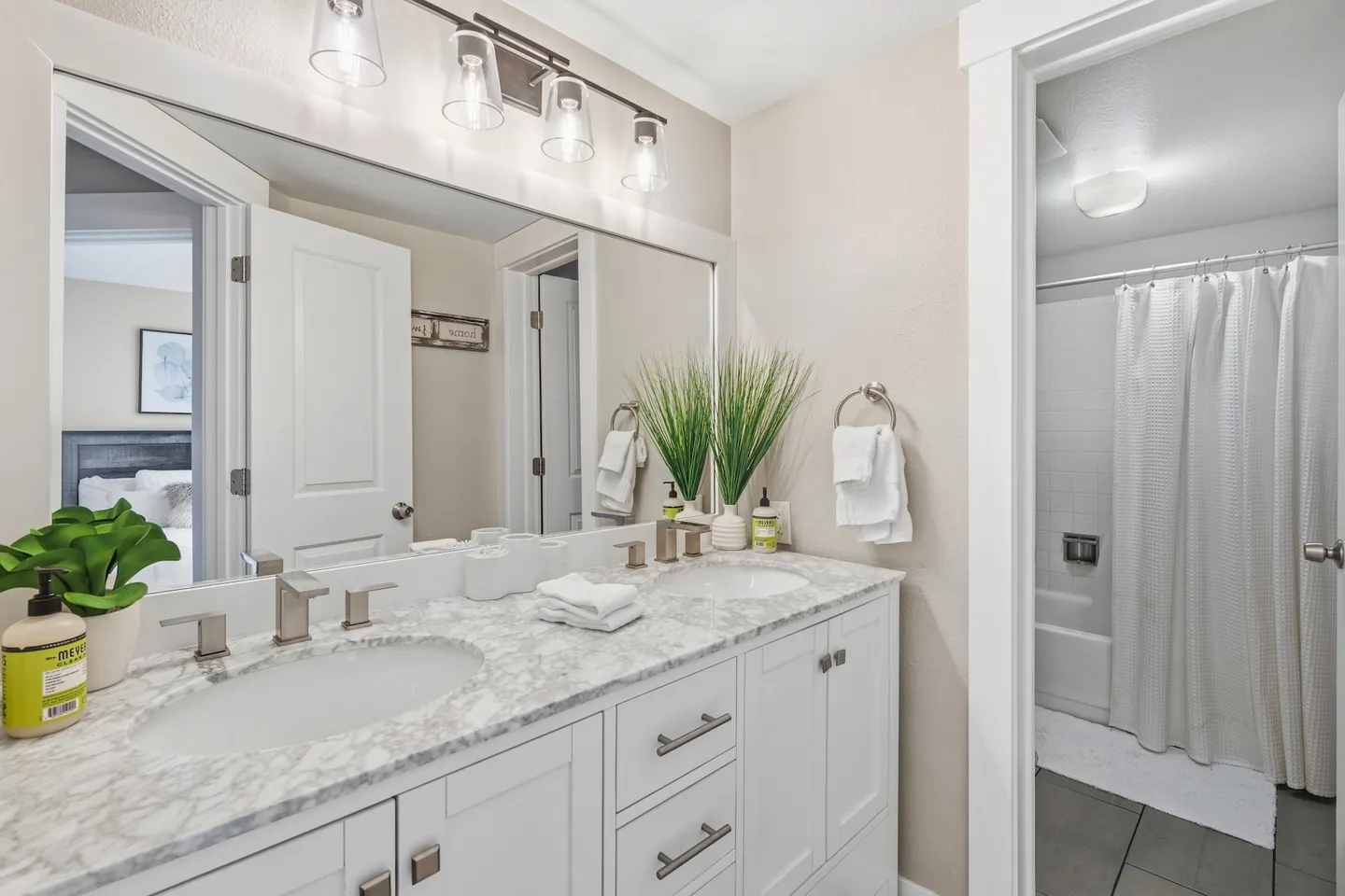 Bathroom with a double-sink vanity, marble-patterned countertop, large mirror, and doorway leading to a shower and tub combination.
