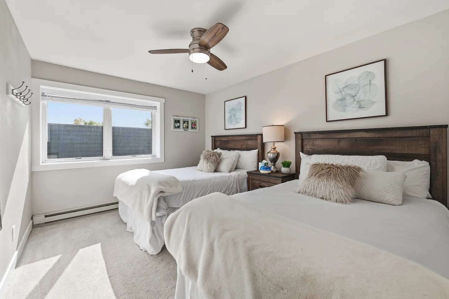 Bedroom with two beds, wooden headboards, light gray carpeting, and a ceiling fan.