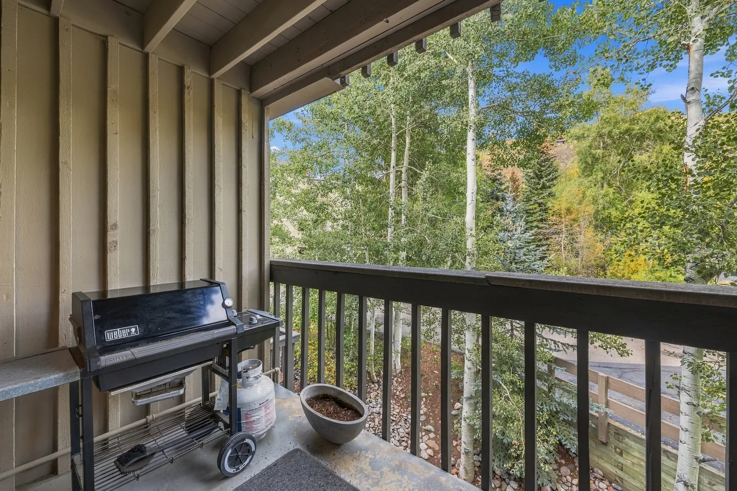 Balcony with a gas grill and wooden railing overlooking aspen and evergreen trees.