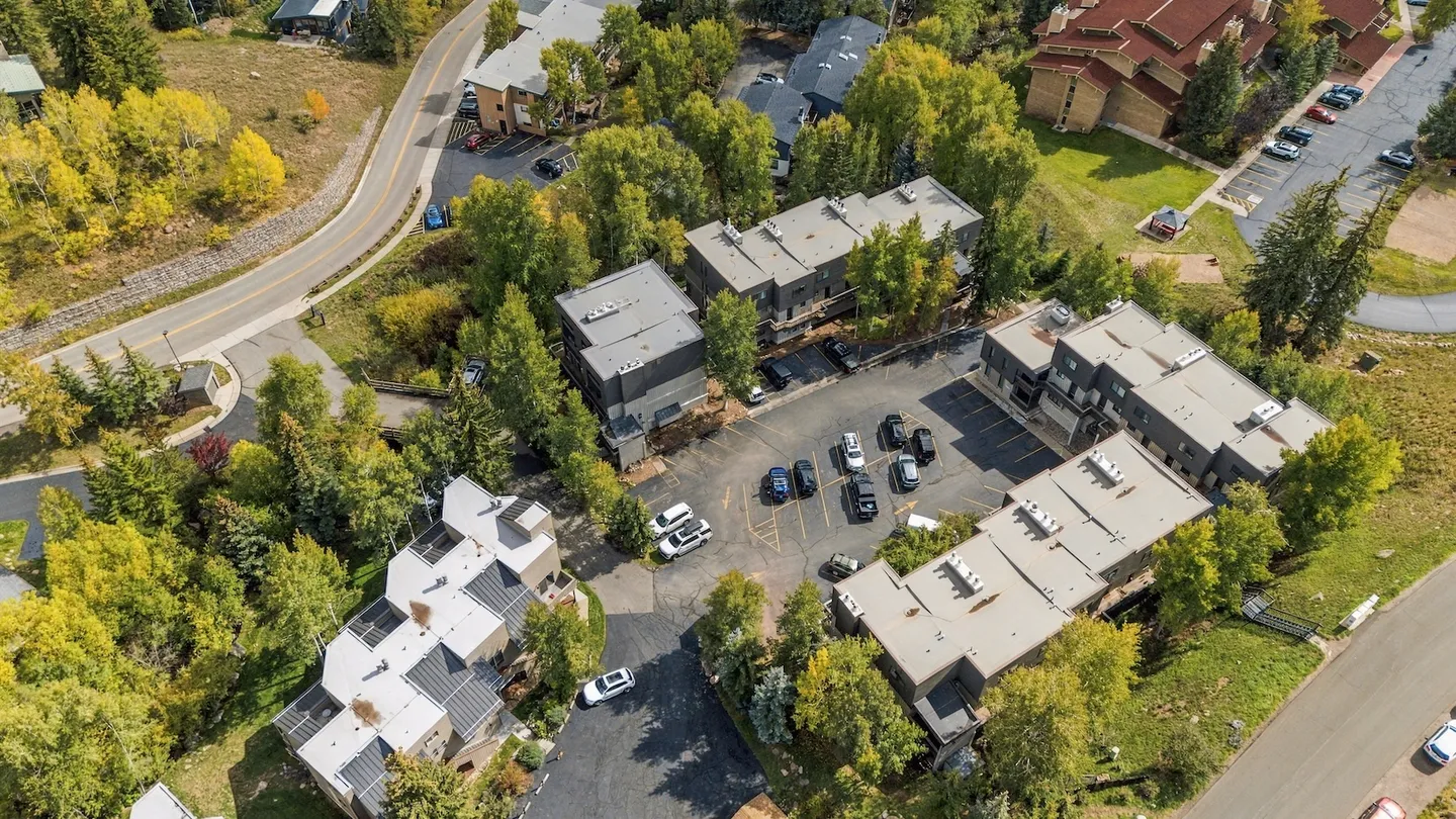 Aerial view of a multi-unit residential complex with parking lots surrounded by green and yellow trees.