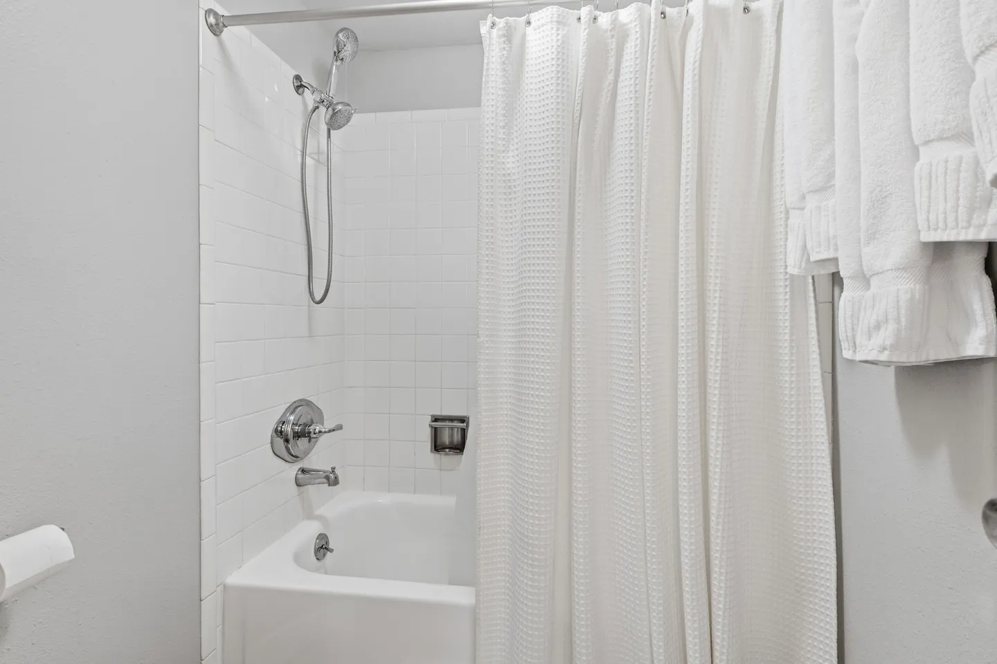 Bathroom tub and shower combination with white tile surround, chrome fixtures, and a white waffle shower curtain.