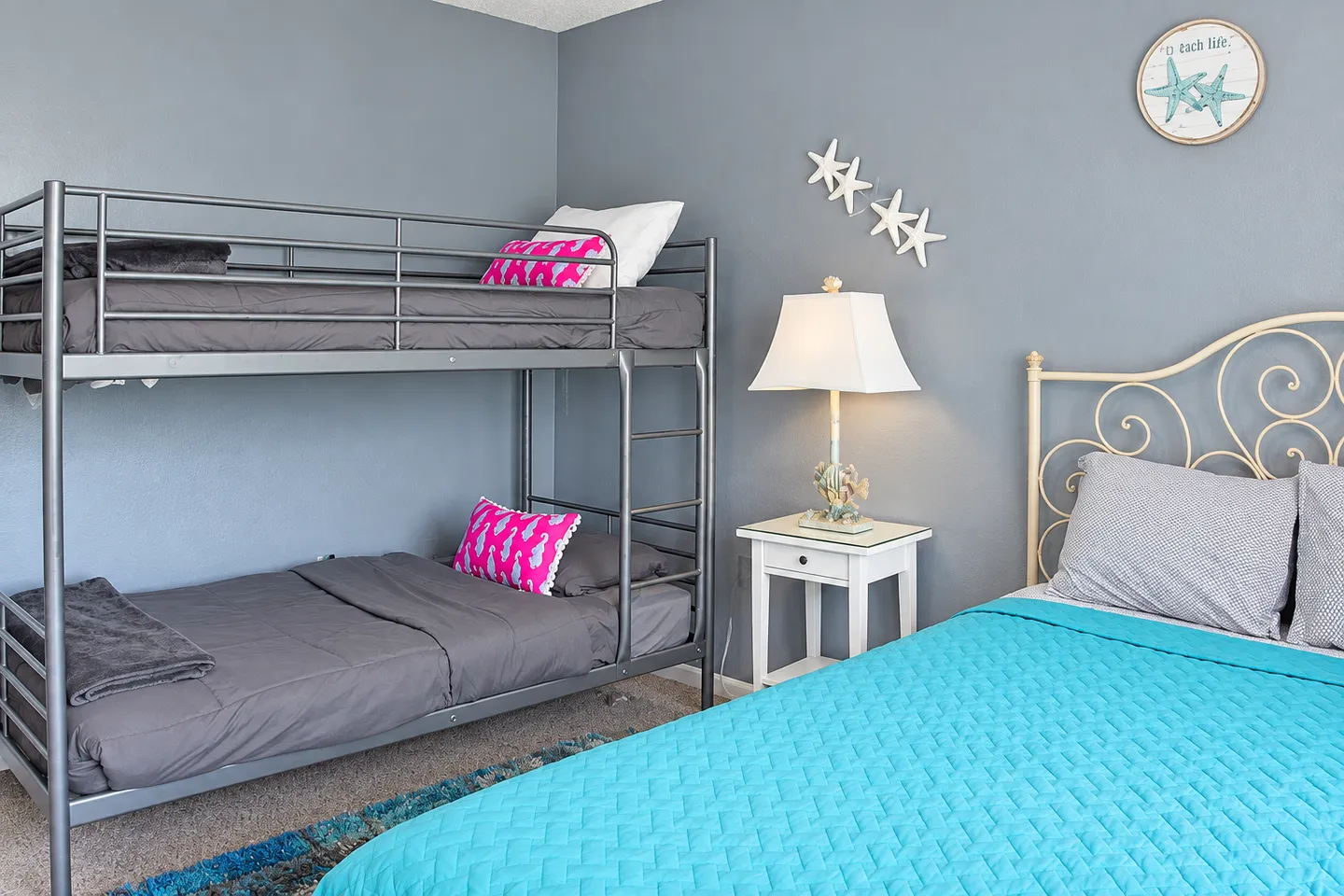 Bedroom featuring a metal bunk bed, a bright blue bedspread on a second bed, and a small white nightstand.