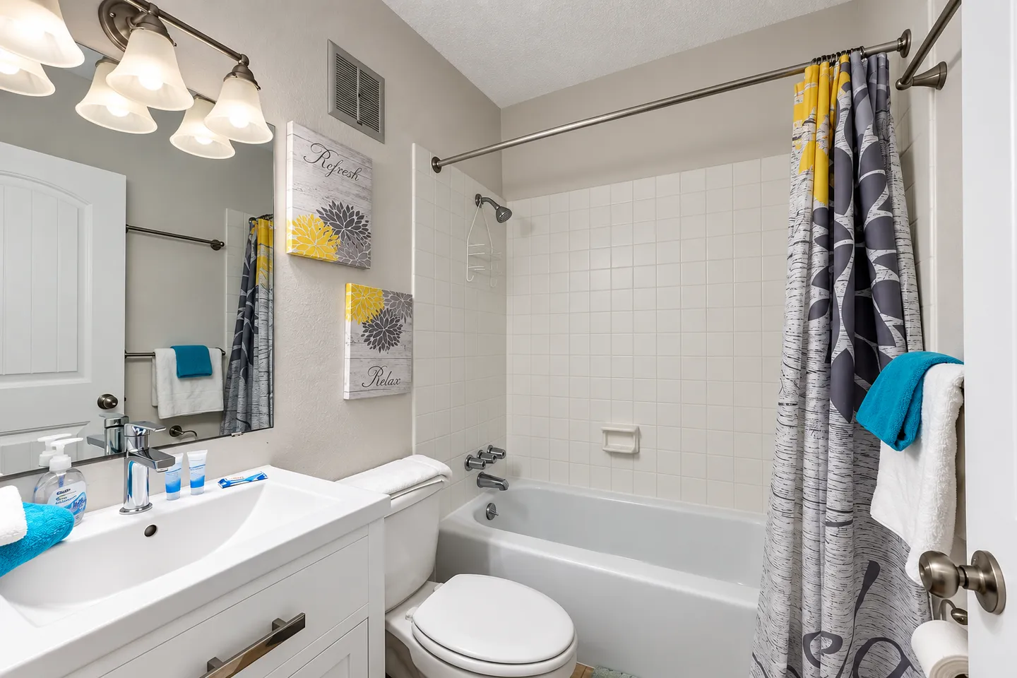 Bathroom with a white vanity, toilet, and bathtub and shower combination surrounded by white tile.