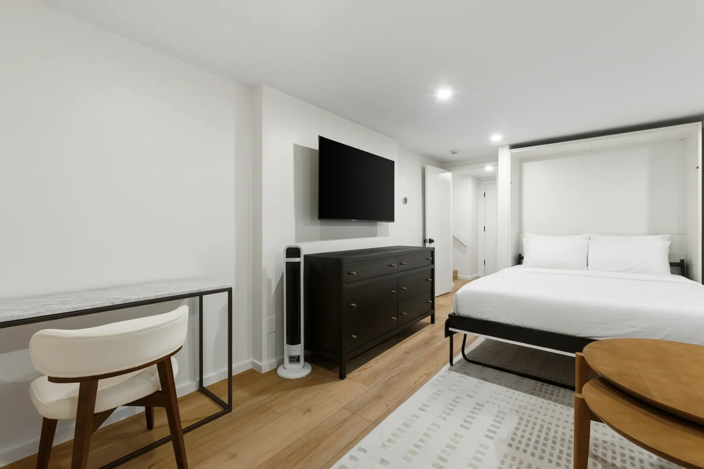 Bedroom with a pull-down wall bed, wall-mounted television, dark wood dresser, and a small desk with a chair.