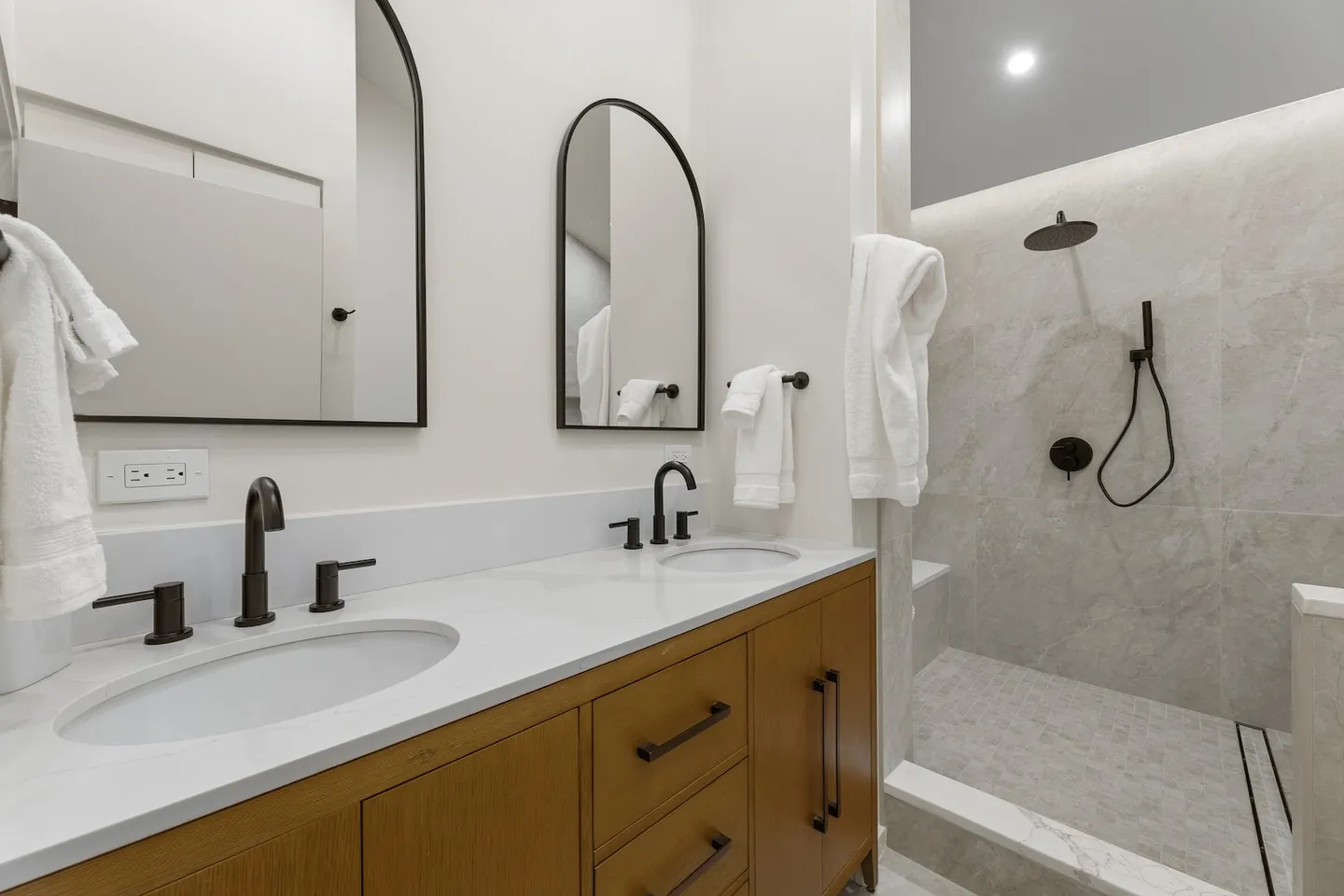 Bathroom with a double-sink vanity, arched black-framed mirrors, matte black fixtures, and a walk-in tiled shower.