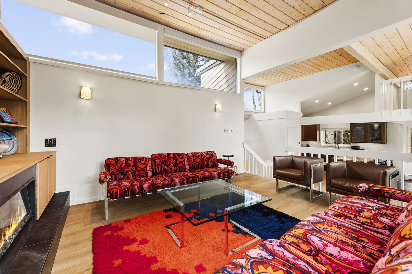 Sunlit living room with wood-paneled ceiling, colorful patterned sofas, clerestory windows, and modern fireplace.
