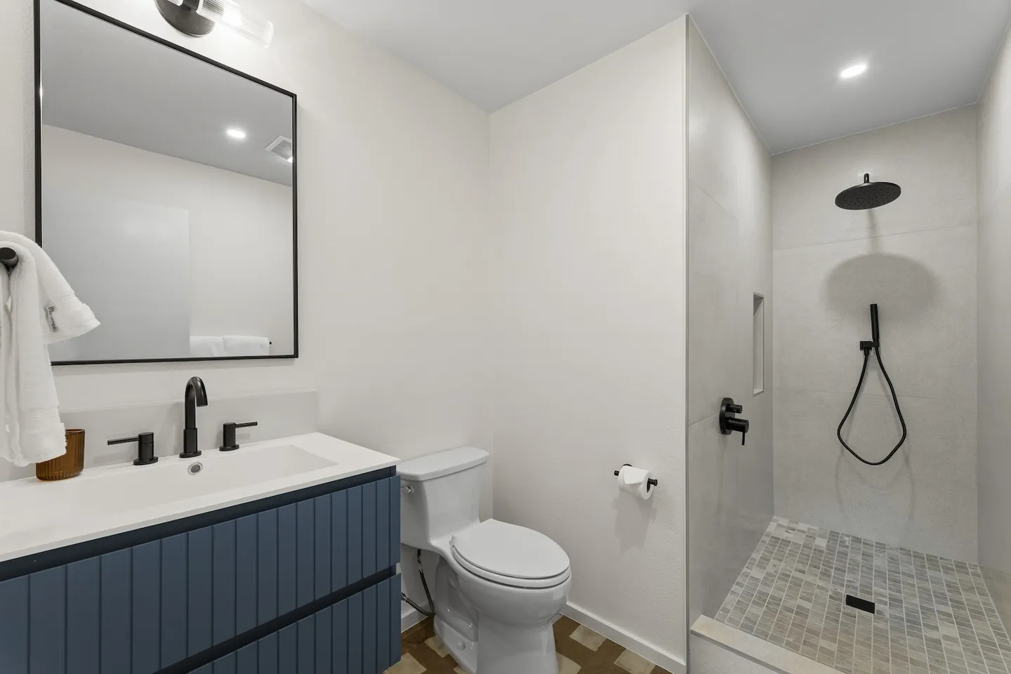 Modern bathroom featuring a blue vanity with black fixtures, a white toilet, and a walk-in shower with tile walls and a handheld showerhead.
