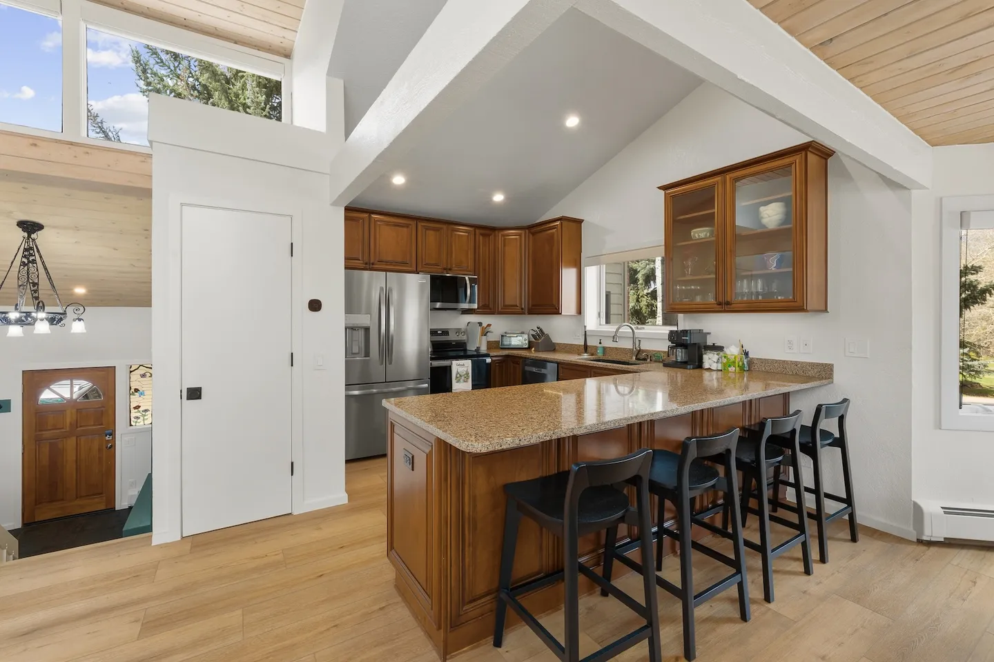 Open concept kitchen with wood cabinets, breakfast bar with black stools, and high vaulted ceilings.