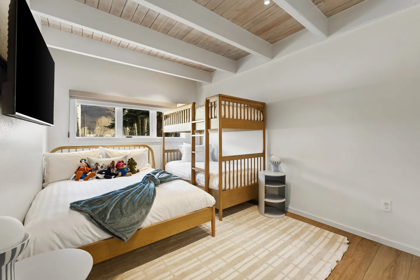 Bedroom with a wood-frame bed, a wooden bunk bed, a beamed ceiling, and a wall-mounted TV.