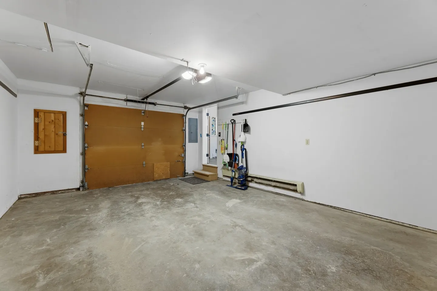 Interior view of an empty garage featuring concrete flooring, a closed garage door, white walls, and an entryway leading into the home.