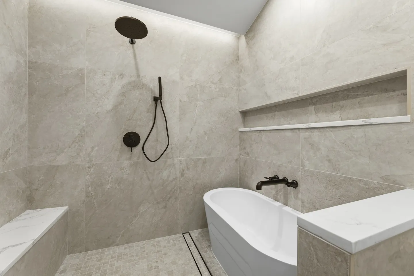 Walk-in wet room shower with tiled walls, an overhead shower fixture, a built-in bench, and a freestanding soaking tub.