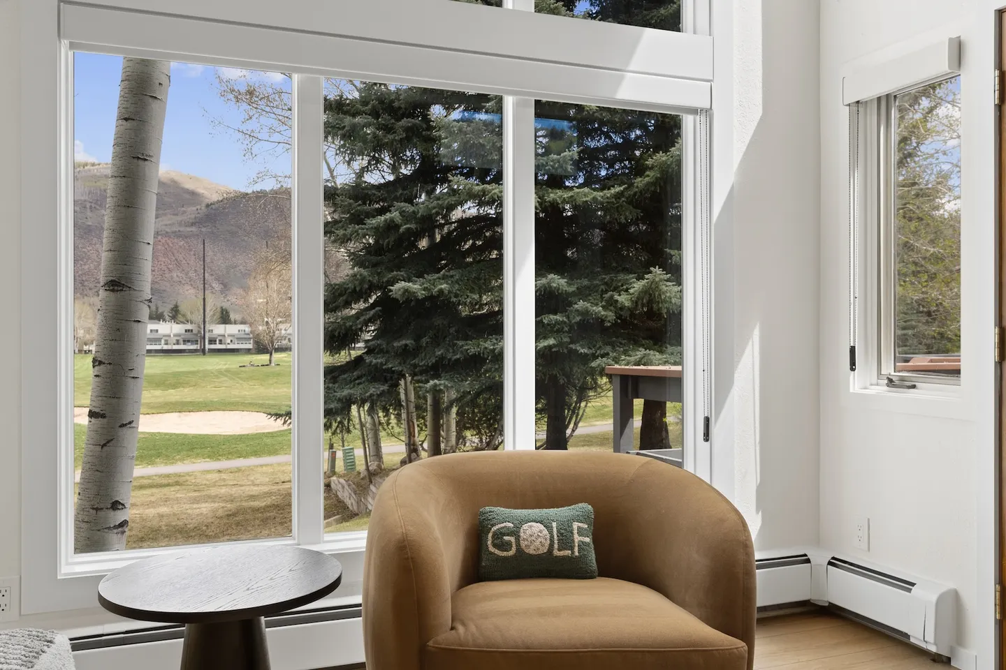 An upholstered armchair beside large picture windows overlooking outdoor trees and distant hills.