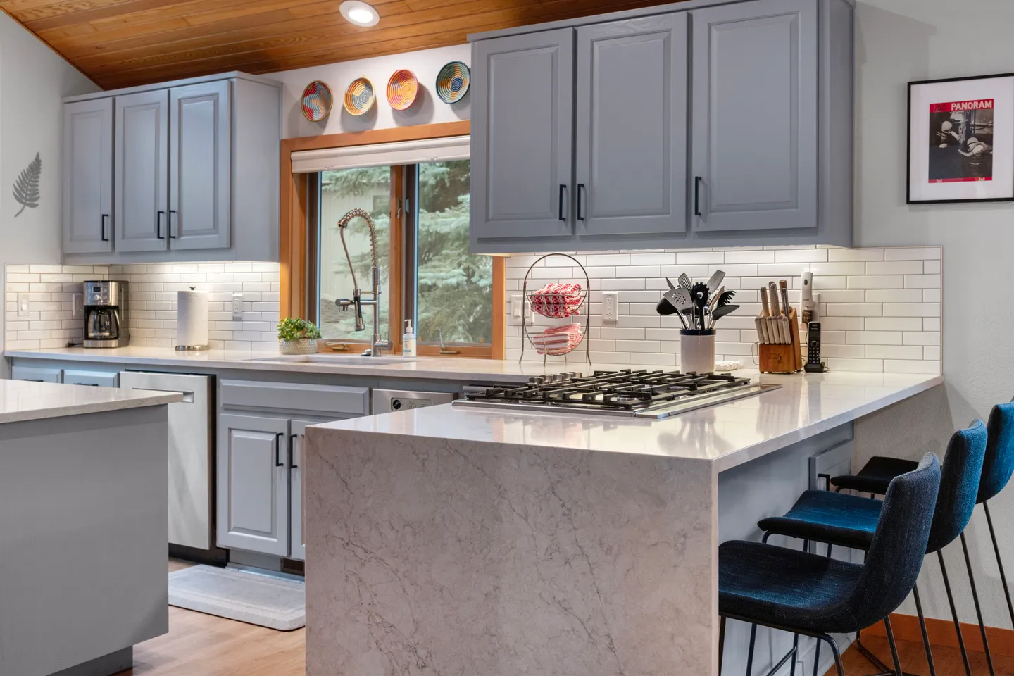 Modern kitchen with grey cabinets, light countertops with a waterfall edge, gas stovetop, and barstools.