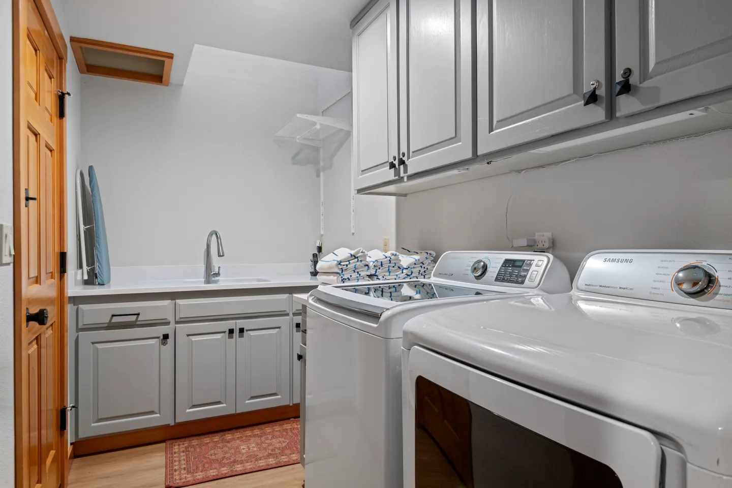 Laundry room with white washer and dryer, utility sink, grey cabinets, and a skylight.