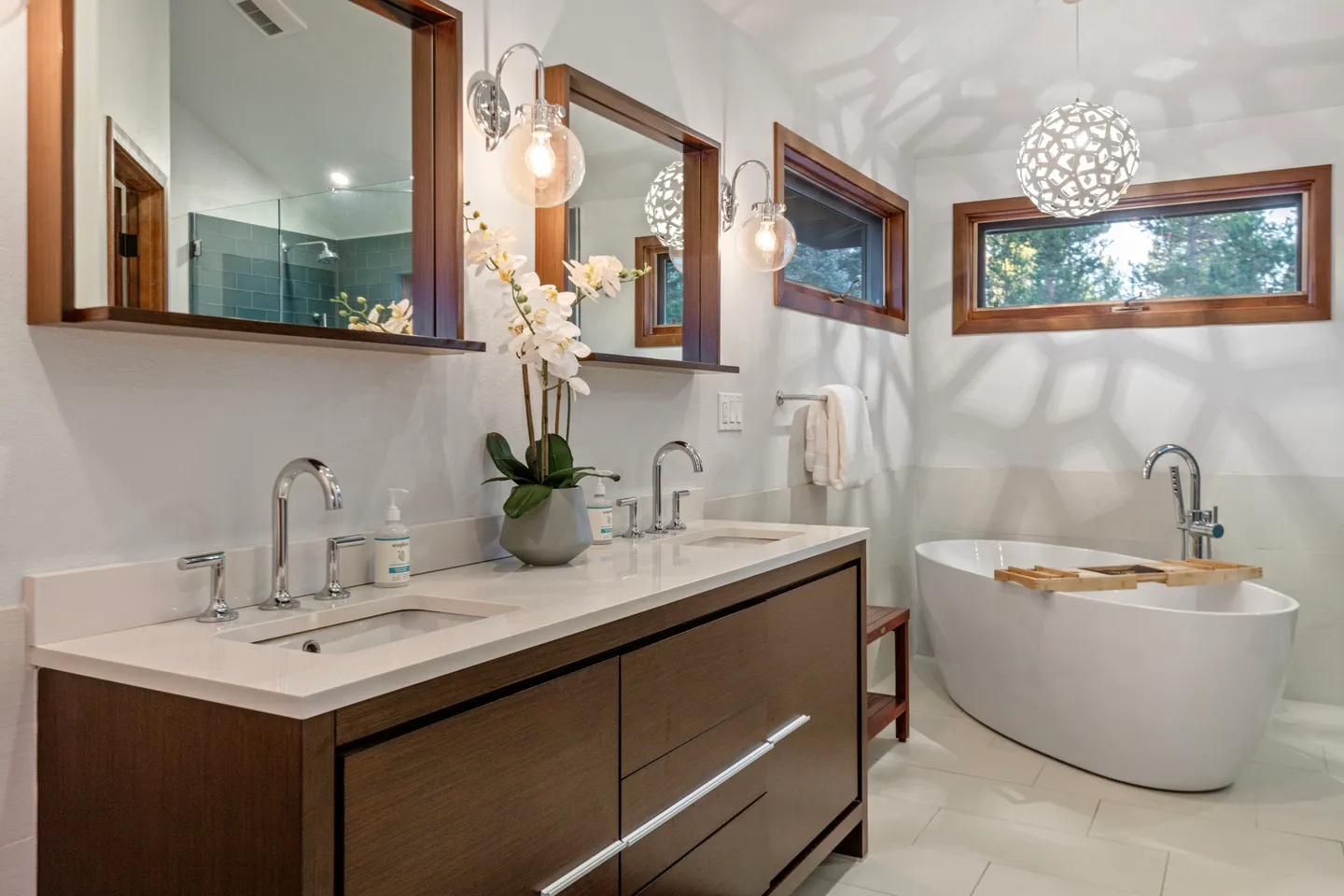 Primary bathroom featuring a double vanity with wooden cabinets, dual framed mirrors, and a freestanding oval soaking tub beside windows.