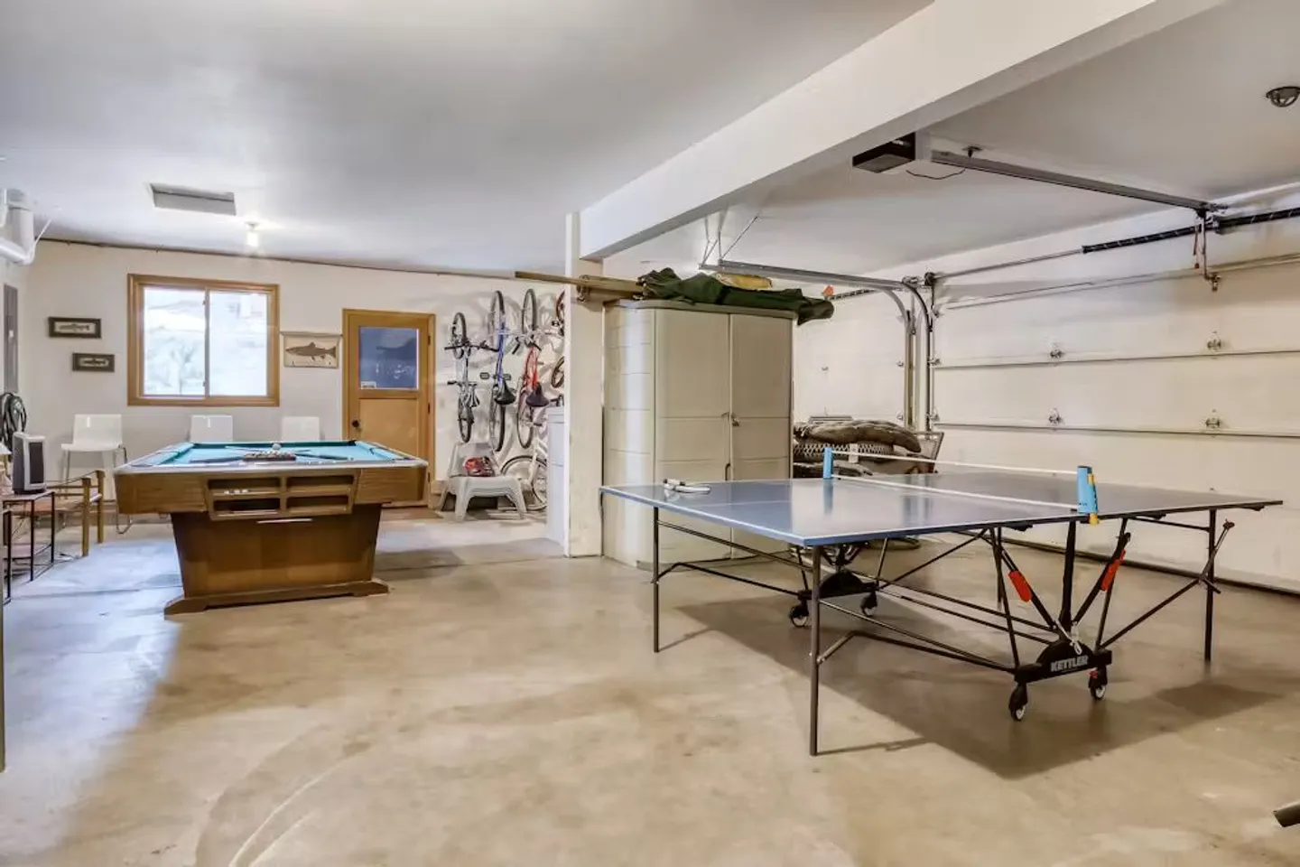A converted garage game room featuring a ping pong table in the foreground and a pool table in the background.