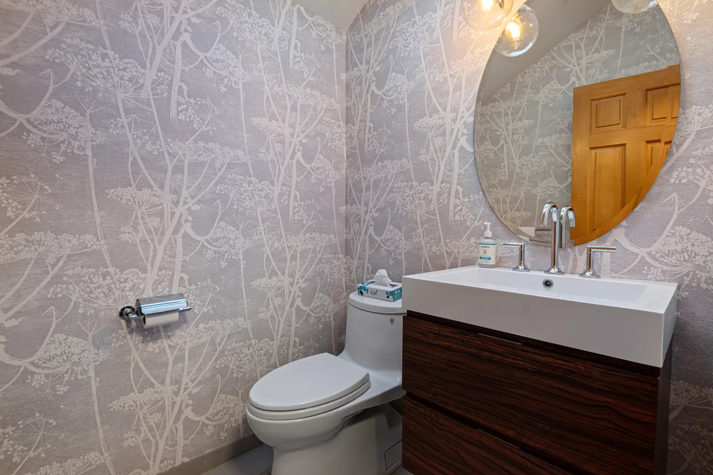 Bathroom featuring patterned botanical wallpaper, a modern floating vanity with a white basin, a white toilet, and a round mirror.