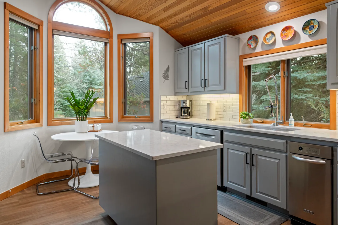 Kitchen with gray cabinetry, a central island, light countertops, wood-paneled ceiling, and a breakfast nook with a round table and windows.