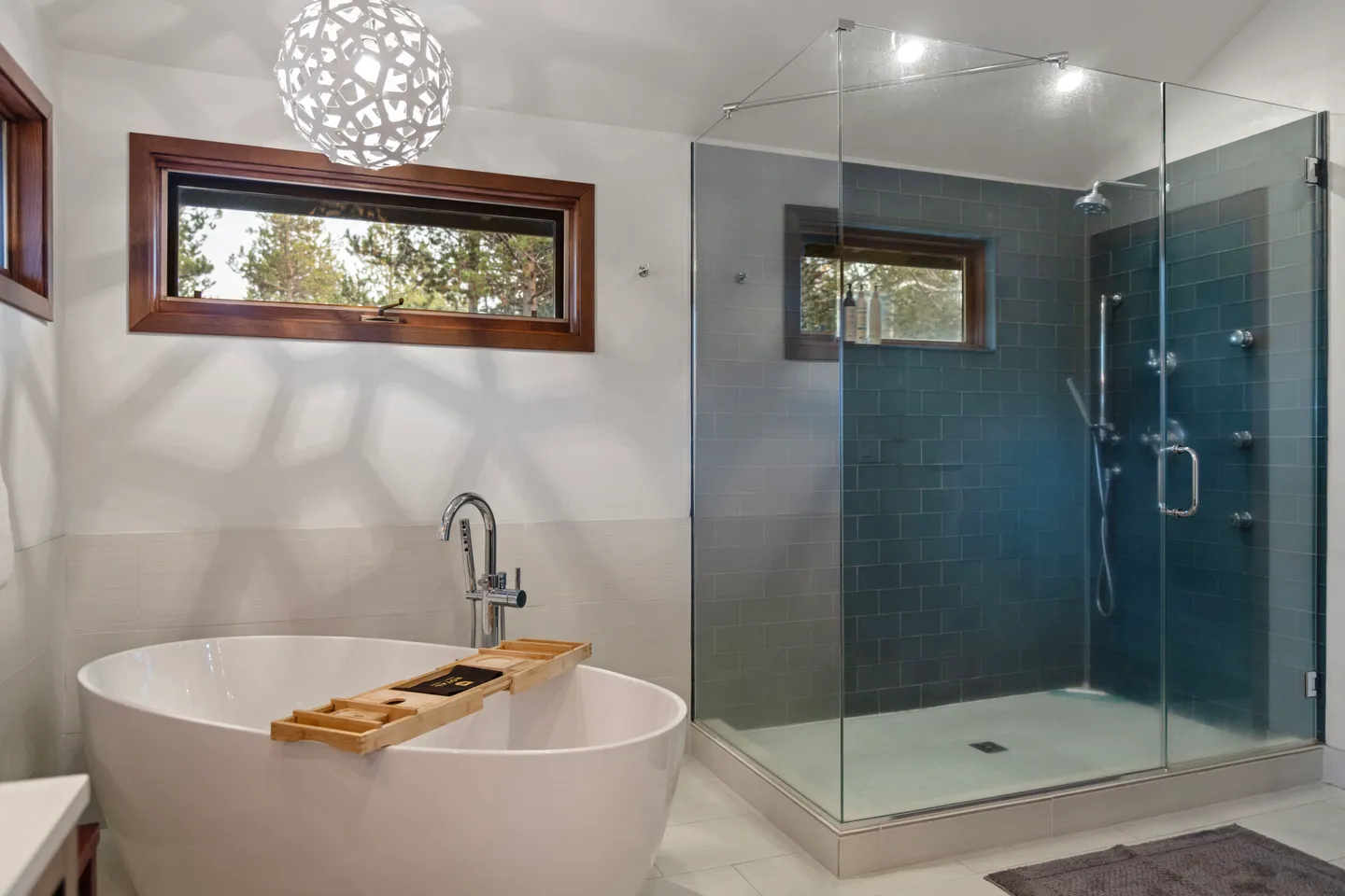 Bathroom with a standalone oval soaking tub and a walk-in glass shower with dark blue tiles.