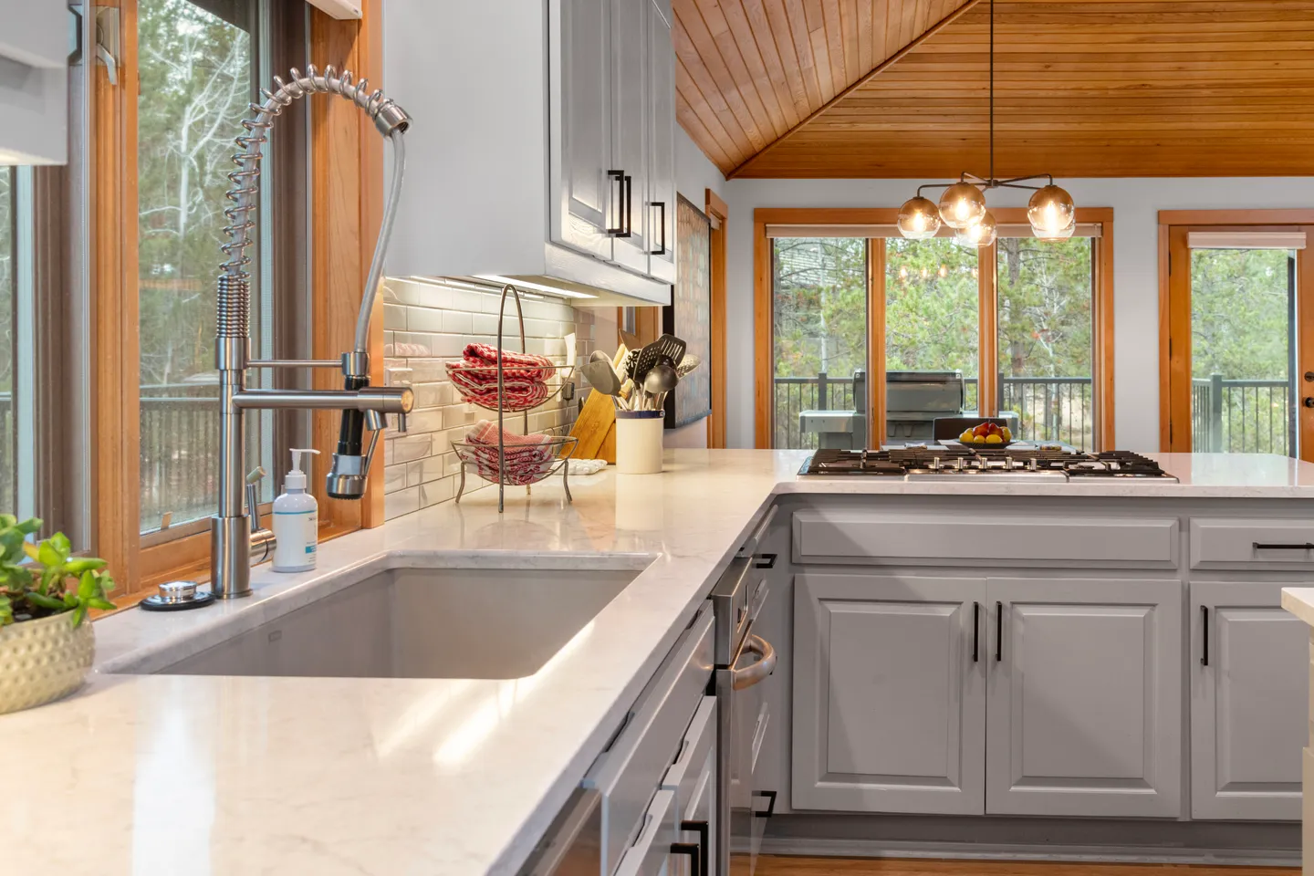 Kitchen counter with undermount sink, commercial-style faucet, light gray cabinetry, and a gas cooktop overlooking outdoor deck windows.