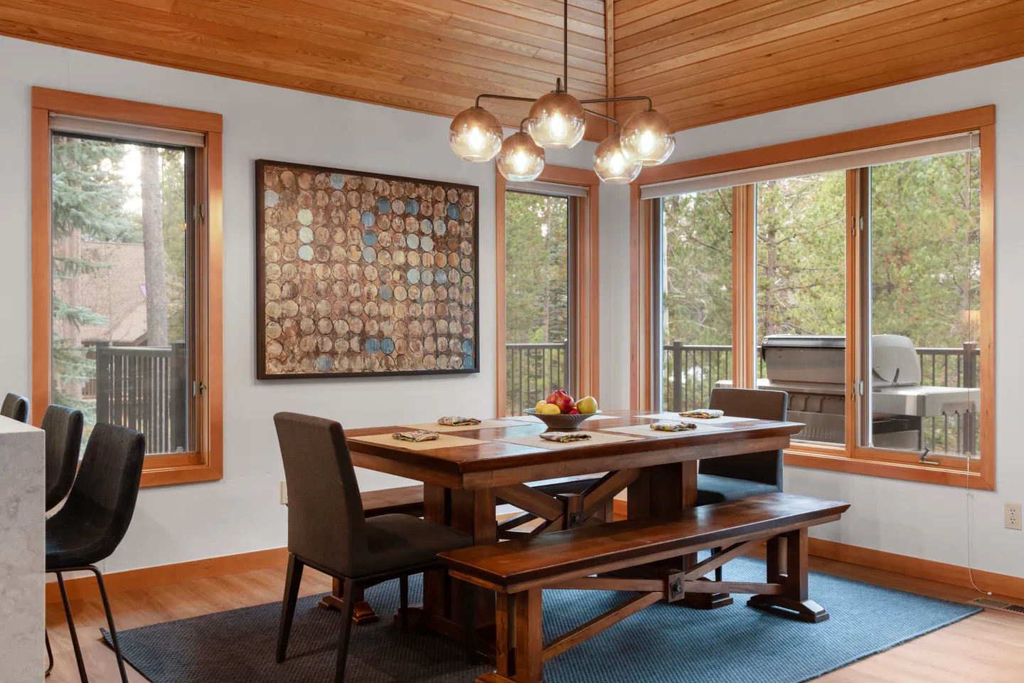 Dining area featuring a wooden table with matching benches, two dark upholstered chairs, and a globe chandelier beneath a wood-paneled ceiling.