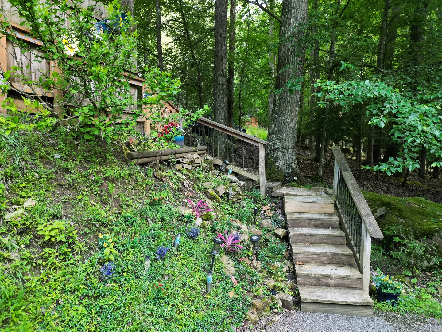 Wooden outdoor stairs with handrails leading up a landscaped wooded slope beside a house.